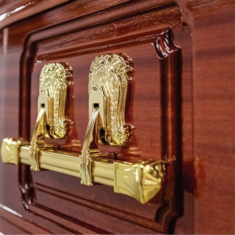 Polished brass bar handles on ornate scroll brackets, mounted on the routed panel side of The Cavendish solid mahogany coffin